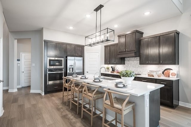 kitchen with decorative backsplash, appliances with stainless steel finishes, a kitchen breakfast bar, and dark brown cabinets