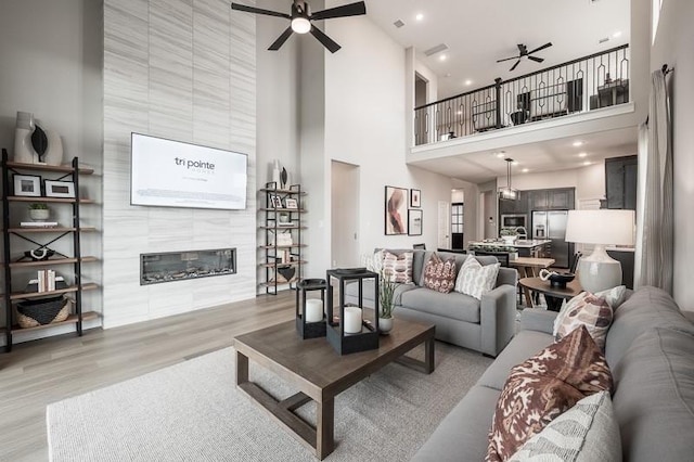 living area with light wood-style flooring, a fireplace, and a ceiling fan