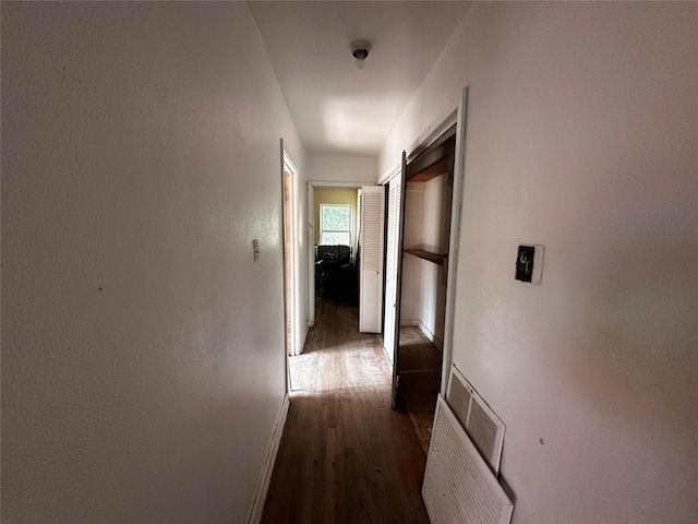 hallway featuring baseboards, visible vents, dark wood-type flooring, and a textured wall