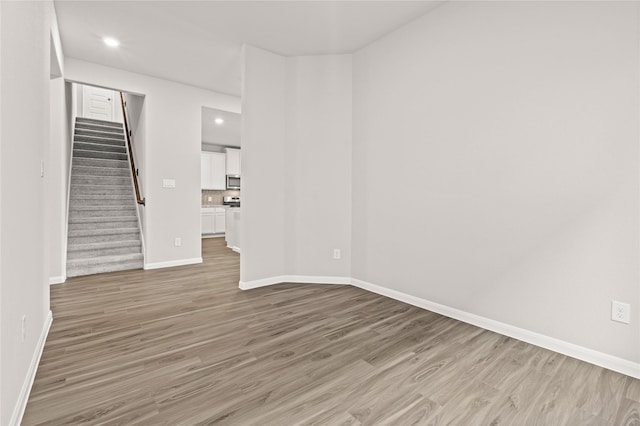 unfurnished living room with stairs, recessed lighting, baseboards, and wood finished floors