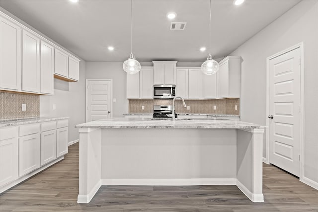 kitchen with visible vents, appliances with stainless steel finishes, light stone countertops, a center island with sink, and pendant lighting