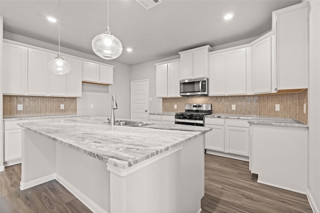 kitchen with a kitchen island with sink, stainless steel appliances, a sink, white cabinetry, and hanging light fixtures