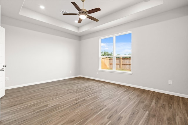 empty room featuring ceiling fan, wood finished floors, a raised ceiling, and baseboards