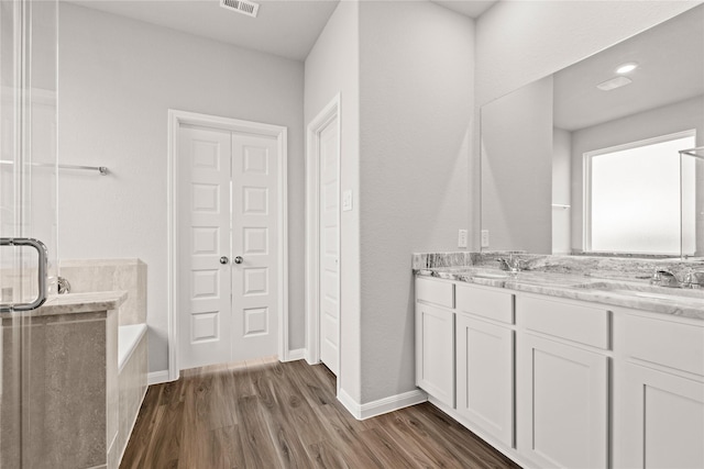 full bathroom with a garden tub, double vanity, visible vents, a sink, and wood finished floors