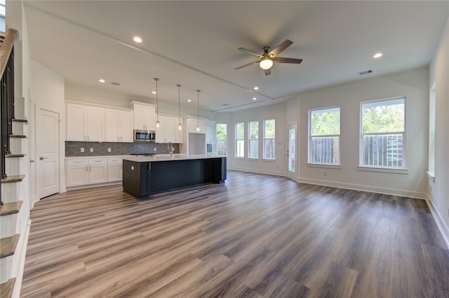 kitchen with stainless steel microwave, hanging light fixtures, open floor plan, white cabinetry, and an island with sink