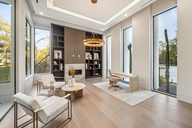 living area with recessed lighting, a high end fireplace, built in features, light wood-type flooring, and a tray ceiling