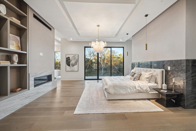 bedroom featuring a chandelier, a tray ceiling, light wood finished floors, and a premium fireplace