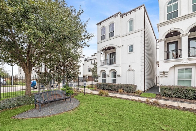 view of front of home featuring fence, a balcony, a front lawn, and stucco siding