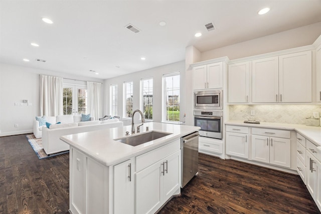 kitchen featuring white cabinets, appliances with stainless steel finishes, open floor plan, light countertops, and a sink