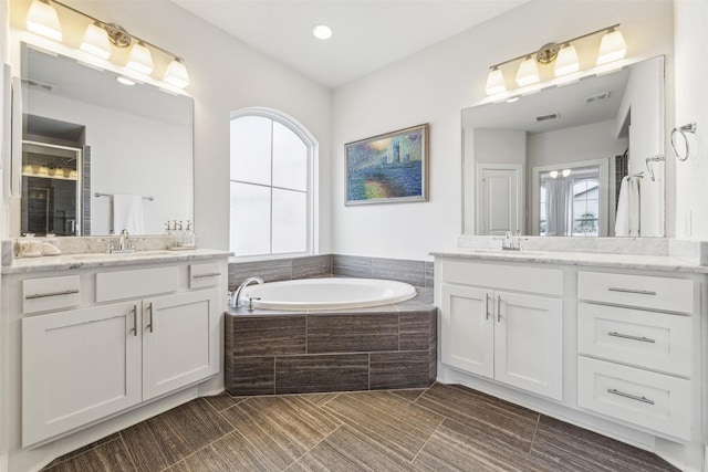 full bathroom featuring a garden tub, visible vents, two vanities, and a sink