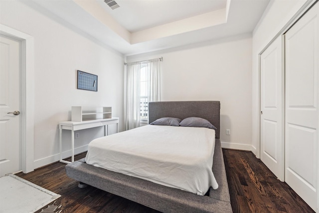 bedroom with a tray ceiling, a closet, visible vents, dark wood-type flooring, and baseboards