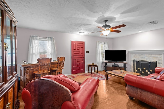 living area with a brick fireplace, visible vents, a textured ceiling, and wood finished floors