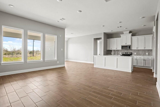 kitchen featuring stainless steel appliances, wood finished floors, white cabinetry, open floor plan, and backsplash