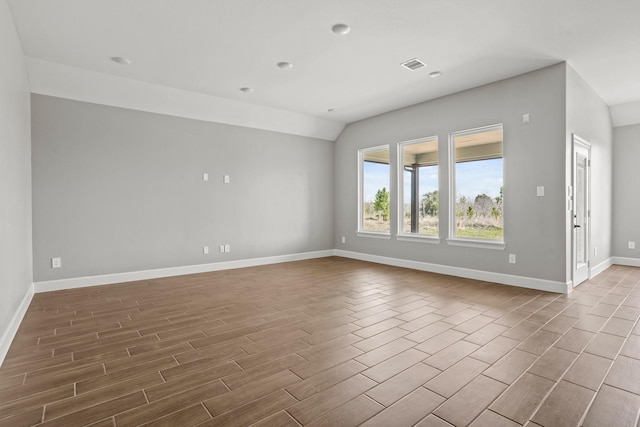 empty room featuring wood tiled floor, visible vents, vaulted ceiling, and baseboards