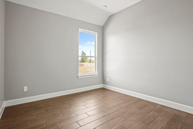 spare room featuring dark wood-type flooring, lofted ceiling, and baseboards