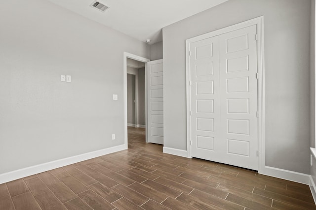 unfurnished bedroom with wood finish floors, a closet, visible vents, and baseboards