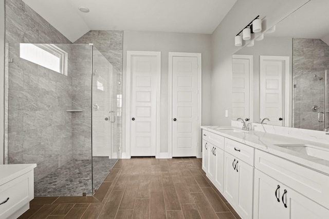 bathroom featuring a stall shower, wood finish floors, a sink, and double vanity