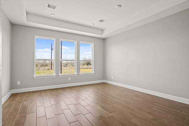 spare room with wood finished floors, visible vents, and baseboards