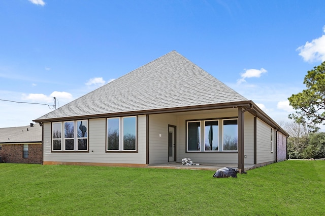 back of property with a shingled roof, a lawn, and a patio area