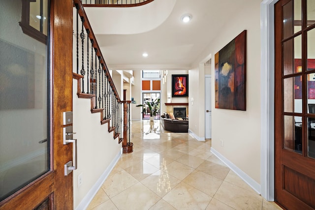 entryway featuring light tile patterned floors, recessed lighting, stairway, a glass covered fireplace, and baseboards