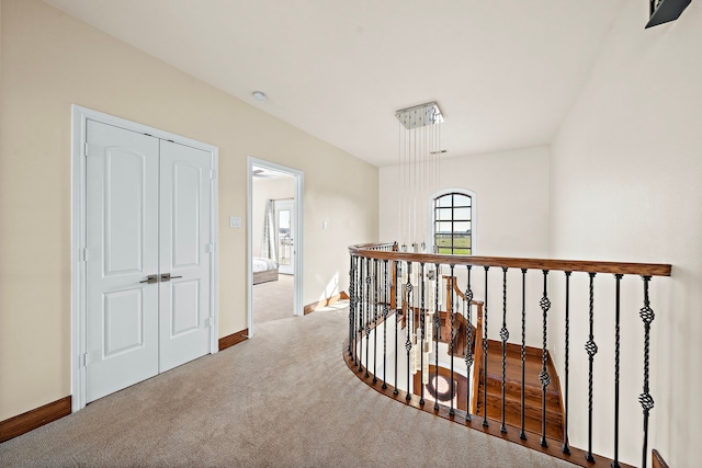 hall with carpet, baseboards, and an upstairs landing