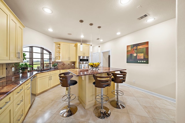 kitchen featuring a breakfast bar area, visible vents, cream cabinetry, decorative backsplash, and a center island