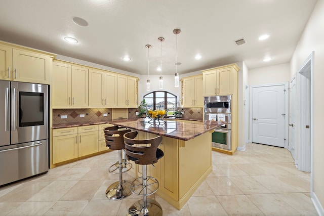 kitchen with a kitchen island, visible vents, appliances with stainless steel finishes, cream cabinetry, and dark stone countertops