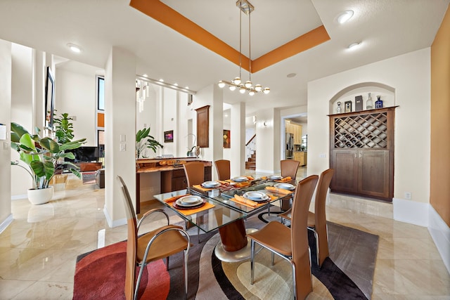 dining area featuring a tray ceiling, marble finish floor, a notable chandelier, stairway, and baseboards