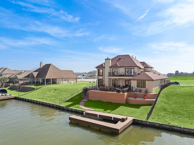 rear view of house with a balcony, a water view, a lawn, and a patio