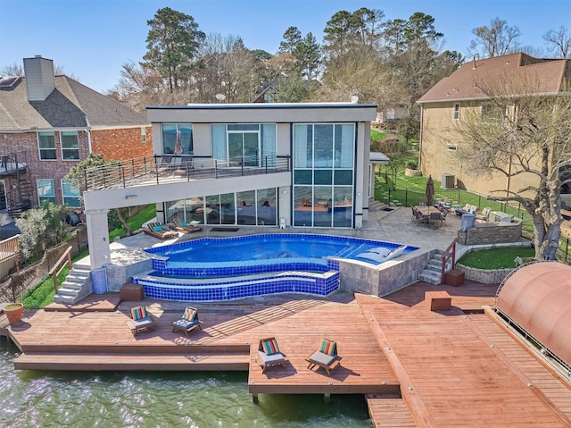 rear view of property featuring a balcony, a patio area, a hot tub, and a deck with water view