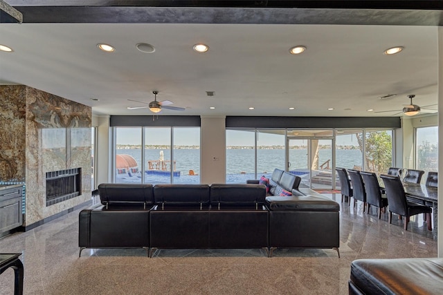 living room with a water view, granite finish floor, a tiled fireplace, and recessed lighting