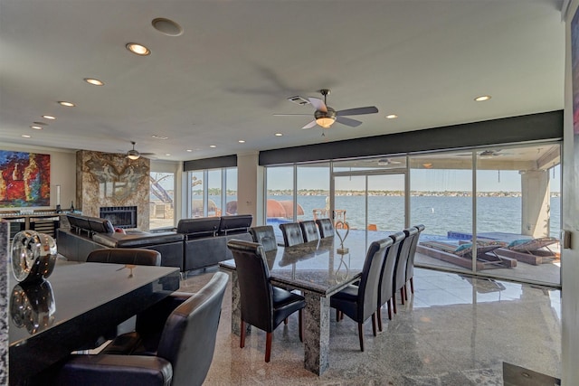 dining area featuring recessed lighting, a water view, granite finish floor, a large fireplace, and ceiling fan