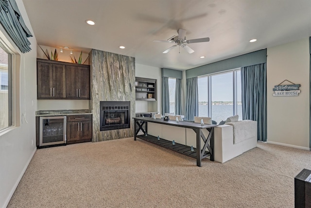 living room featuring wine cooler, a water view, a fireplace, and light colored carpet