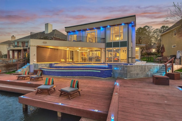 back of house at dusk featuring a bar, a deck with water view, and a balcony