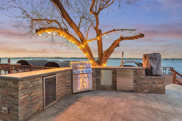 patio terrace at dusk featuring exterior kitchen and a water view