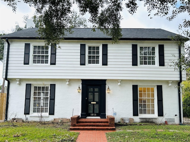 colonial-style house featuring entry steps, a front lawn, and brick siding