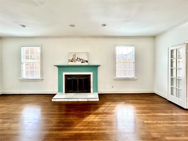 unfurnished living room featuring dark wood-style floors, ornamental molding, a wealth of natural light, and a glass covered fireplace