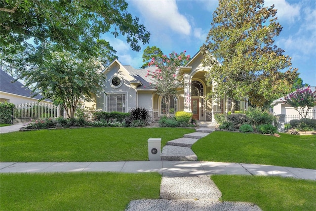 view of property hidden behind natural elements featuring stucco siding, fence, and a front yard