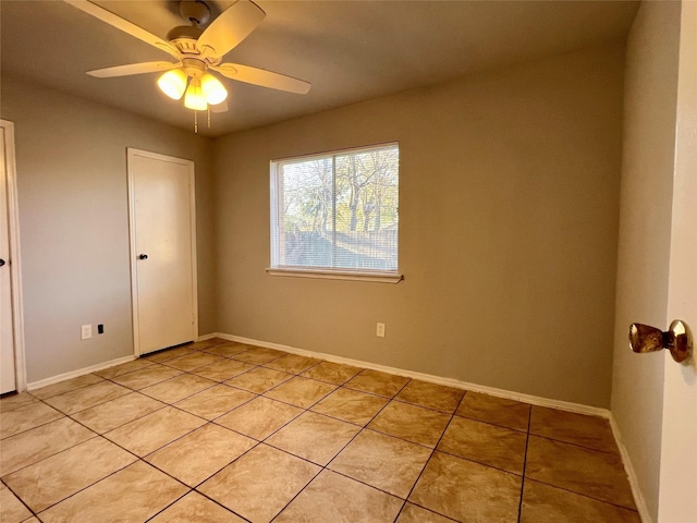 empty room with light tile patterned floors, a ceiling fan, and baseboards