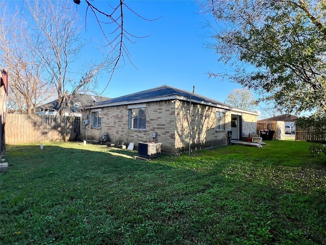 view of side of property featuring central AC, brick siding, a lawn, and fence