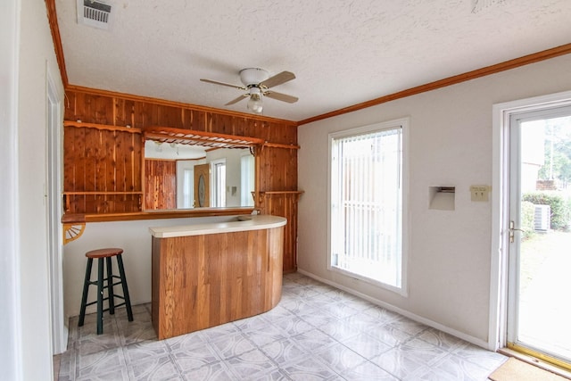 kitchen with light floors, visible vents, ornamental molding, ceiling fan, and a textured ceiling