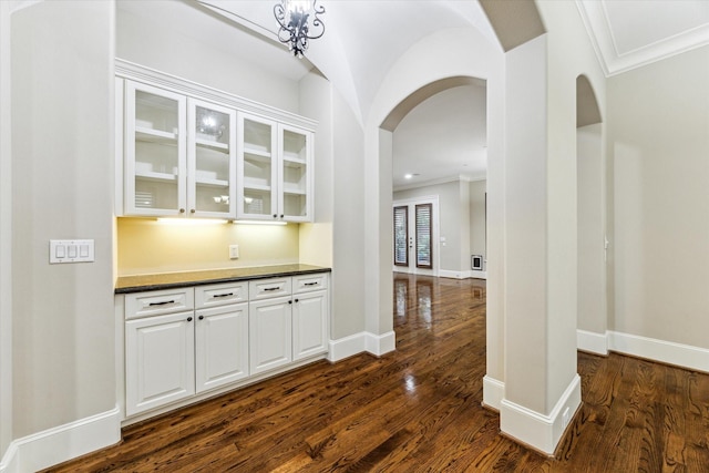 bar with dark wood-style floors, arched walkways, and ornamental molding