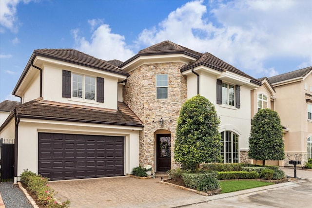 view of front facade with a garage, stone siding, decorative driveway, and stucco siding