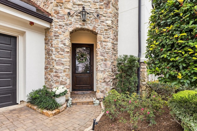 entrance to property featuring a garage, stone siding, and stucco siding