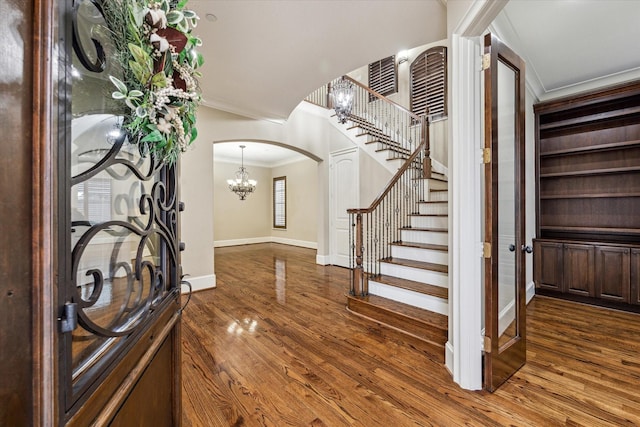 entrance foyer with arched walkways, dark wood-type flooring, baseboards, stairs, and ornamental molding