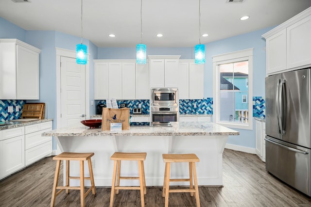 kitchen with stainless steel appliances, a kitchen island, white cabinetry, hanging light fixtures, and light stone countertops