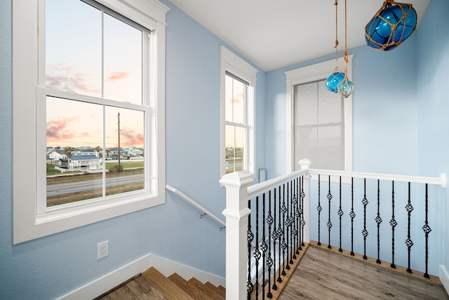 hall featuring baseboards, wood finished floors, and an upstairs landing