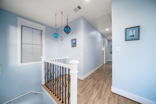 corridor featuring light wood finished floors, visible vents, attic access, an upstairs landing, and baseboards