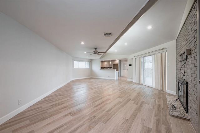 unfurnished living room featuring visible vents, light wood-style floors, a ceiling fan, a brick fireplace, and baseboards