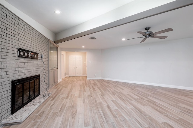 unfurnished living room with light wood finished floors, baseboards, a brick fireplace, and visible vents